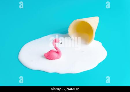 Figurine rose flamant dans un flaque de glace à cornet de gaufres fondu isolé sur fond bleu. Arrière-plan d'été rafraîchissant. Banque D'Images