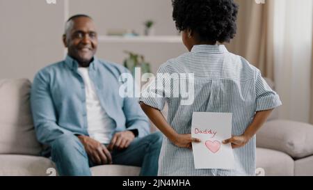 Famille afro-américaine père mûr assis à la maison sur un canapé surprise acceptant les voeux d'anniversaire petite fille aimante donne main carte pour Banque D'Images