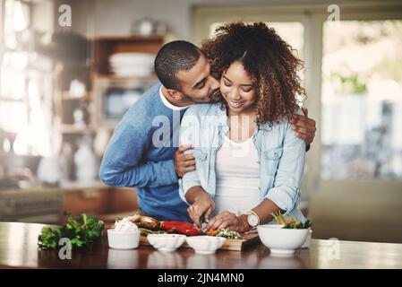 Romantique, amoureux et attentionné petit ami embrasse sa petite amie et montre de l'affection pendant qu'ils font la nourriture dans la cuisine. Un couple partage un baiser et un hug Banque D'Images