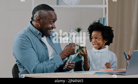 Le père américain africain aide à faire des devoirs enseigne l'arithmétique de petite fille en utilisant des billets en dollars enfant fille apprend à compter papa montre de l'argent papier Banque D'Images