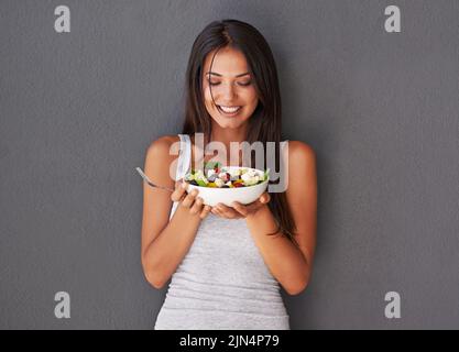 Une jeune femme en bonne santé mangeant son saladier frais. Souriante belle femme tenant et appréciant manger son propre plat vert de régime de légumes comme Banque D'Images