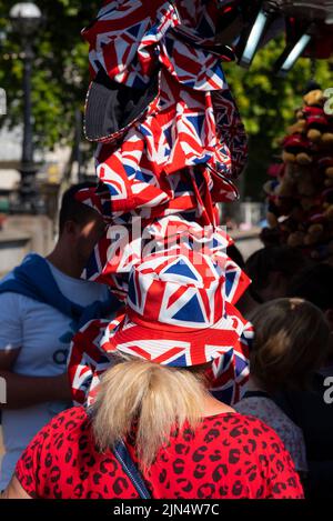 Une femme essayant un chapeau de soleil sur le thème du drapeau de l'Union Jack dans une boutique de souvenirs touristiques à Westminster, Londres, Royaume-Uni. Chapeau de protection patriotique Banque D'Images