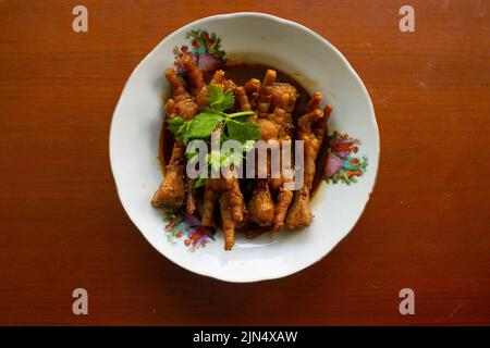 Pieds de poulet épicés au céleri, au piment, à l'oignon et à l'ail servis avec une assiette blanche isolée d'un fond noir. Banque D'Images