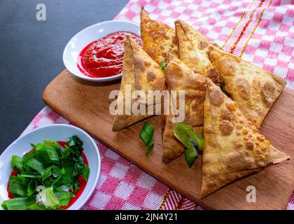 Samosa, samsa ou somsa sont des pâtisseries frites triangulaires ou pastri servies avec une sauce tomate et une tranche de poireaux, sur fond noir Banque D'Images