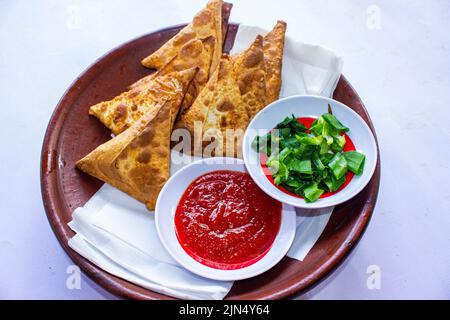 Samosa, samsa ou somsa sont des pâtisseries frites triangulaires ou pastri servies avec une sauce tomate et une tranche de poireaux, sur fond noir Banque D'Images