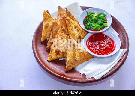 Samosa, samsa ou somsa sont des pâtisseries frites triangulaires ou pastri servies avec une sauce tomate et une tranche de poireaux, sur fond noir Banque D'Images