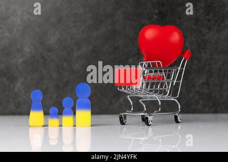 Quatre petites figurines en bois bleu jaune représentant une famille - mère, père et deux enfants - près d'une épicerie avec un grand coeur rouge. Concept de Banque D'Images