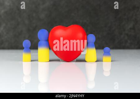 Quatre petites figurines en bois bleu jaune qui symbolisent une famille - une mère, un père et deux enfants, debout près d'un grand coeur rouge. Le concept de f Banque D'Images