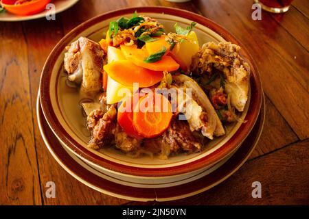 Délicieuse soupe de côtes ou soupe IGA dans un bol servi avec des carottes de pommes de terre et du céleri sur fond de bois Banque D'Images