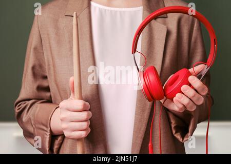 Femme enseignante tenant des écouteurs rouges dans ses mains sur un tableau noir de l'école dans la salle de classe Banque D'Images