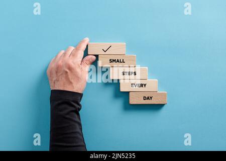 La main masculine arrange une échelle en bois avec le message petits pas chaque jour. Concept de réussite commerciale, de réalisation d'objectifs et de vision de carrière. Banque D'Images