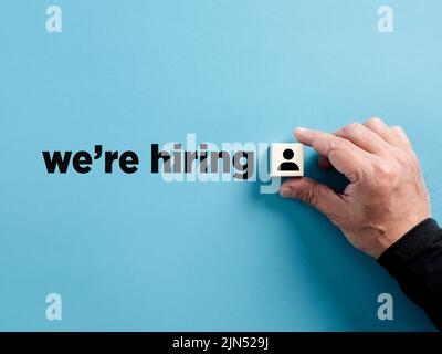 La main masculine met un cube en bois avec le symbole de l'employé à côté du message que nous embauchons. Annonce d'emploi ou de recrutement. Banque D'Images