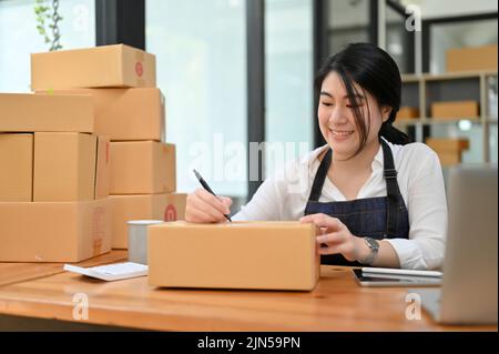 Belle jeune asiatique e-commerce startup entrepreneur préparant ses paquets d'expédition dans le bureau. Banque D'Images