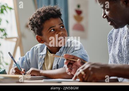 Un écolier africain écoutant son professeur expliquant un nouveau sujet à table pendant la scolarisation à domicile Banque D'Images