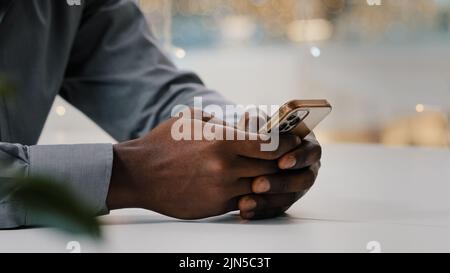 Gros plan hommes dactylographiant sur un téléphone mobile homme d'affaires afro-américain méconnaissable vérifiant les e-mails à distance en utilisant un smartphone jeune homme Banque D'Images