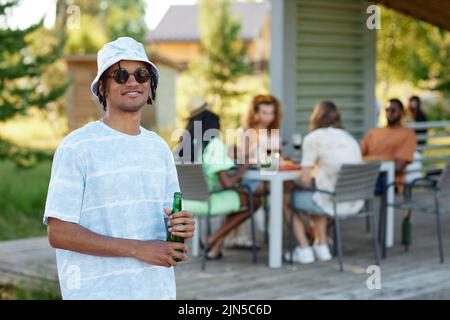 Portrait à la taille du jeune homme noir portant des lunettes de soleil souriant à l'appareil photo et tenant un verre pendant la fête en plein air avec des amis en été, espace de copie Banque D'Images