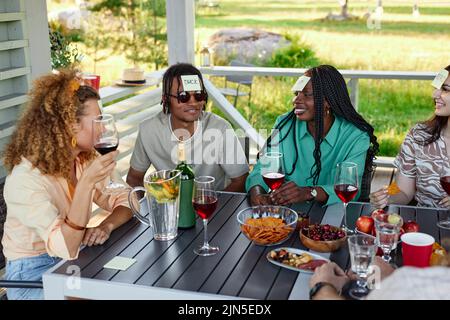 Groupe diversifié de jeunes jouant à deviner qui jeu en étant assis à table dehors en été Banque D'Images