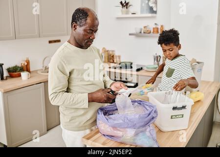 Père africain séparant les ordures dans le paquet et les conteneurs avec son fils dans la cuisine à la maison Banque D'Images