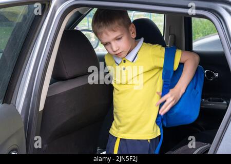 Portrait d'un garçon souriant avec un sac d'école sortant de la voiture. Prendre un étudiant après l'école. Le garçon entre dans la voiture. Banque D'Images