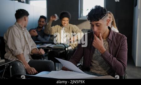 L'étudiant de Nerd est assis dans une salle de classe à un bureau seul lit le résumé souffre d'une attitude agressive cruelle de la part des camarades de classe le jeune gars perdant se sent victime de Banque D'Images