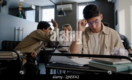 Triste inquiet contrarié déçu étudiant caucasien nerd portant des lunettes assis dans la salle de classe au bureau seul prépare pour la leçon lit des notes agressive en colère Banque D'Images