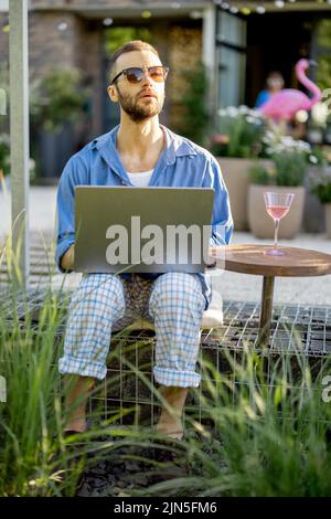 L'homme travaille sur un ordinateur portable tout en étant assis à l'arrière-cour Banque D'Images