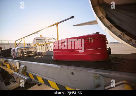 Chargement des bagages dans l'avion. Valise rouge sur le tapis roulant de l'aéroport. Banque D'Images