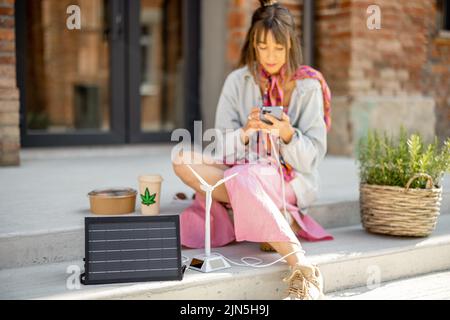 Une femme recharge son téléphone à partir d'un panneau solaire portable Banque D'Images