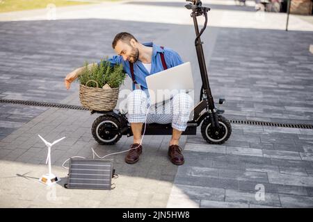 L'homme travaille sur un ordinateur portable tout en étant assis sur un scooter électrique à l'extérieur Banque D'Images