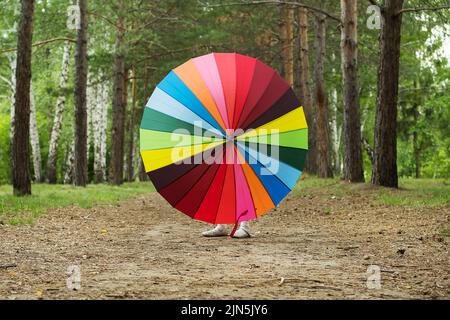 Bonne fille drôle tenant parapluie arc-en-ciel. Adorable écolière joyeuse jouant dans un parc d'été pluvieux. Enfant marchant dans la douche d'automne. Des activités de plein air Banque D'Images