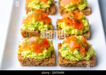 Toasts à l'avocat et saumon fumé sur l'assiette en bois Banque D'Images