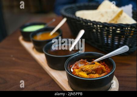 Trempette indienne, relish, chutney et sauce servis dans de petits bols noirs avec du pain de papadam croustillant sur une table en bois sombre, espace de copie, sélection de foyer, très n Banque D'Images