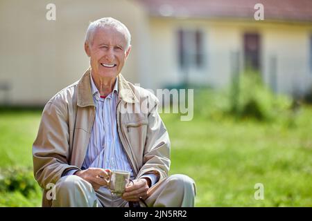 Sourire éclatant homme âgé de 75 ans assis à l'extérieur devant sa maison. Banque D'Images