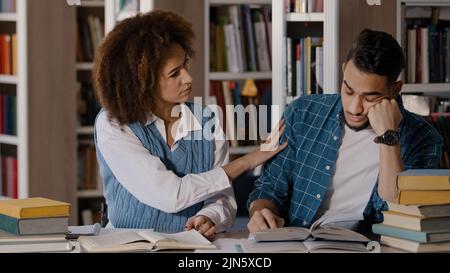 Deux étudiants gars et fille assis à la salle de classe de bureau écrit des notes dans le bloc-notes écrivant l'information de livre de lecture de manuel de jeunes hommes étudiant tombe Banque D'Images