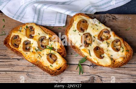 Sandwich toasté à base de pain au levain traditionnel avec fromage et champignons bruns assaisonnés d'herbes de romarin sur une planche de bois, vue du dessus Banque D'Images