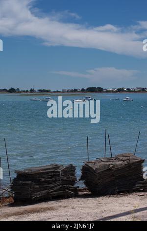 Les bateaux à moteur sont amarrés dans un point d'entrée calme. Le ciel est bleu le temps est beau avec le vent. Des sacs d'huîtres sont empilés au premier plan. Banque D'Images