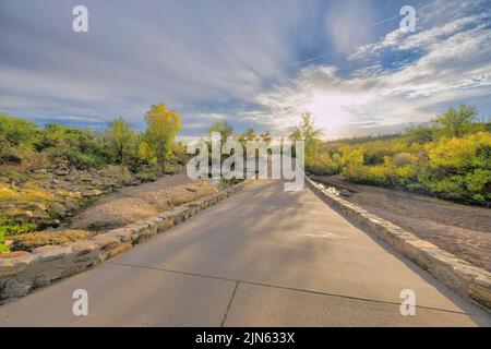 Pont en pierre au-dessus d'une crique dans le parc national de Sabino Canyon à Tucson, Arizona. Pont en béton avec vue sur les plantes vertes du désert et le ciel du coucher du soleil. Banque D'Images