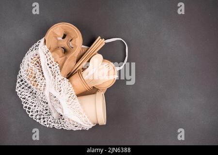 Ustensiles en papier dans un sac en coton blanc sur fond de béton foncé avec espace de copie - gobelets en papier, récipients à nourriture et couverts en bambou en bois. Soutien Banque D'Images