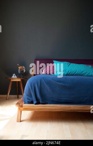 Vue verticale d'une chambre moderne et confortable avec un lit bleu et rouge à côté d'une petite table contre le mur gris Banque D'Images