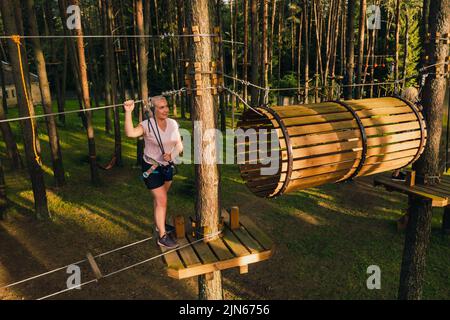 Une femme surmonte un obstacle dans une ville de corde. Une femme dans un parc de corde de forêt. Banque D'Images