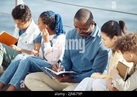 Portrait d'un enseignant masculin souriant avec un groupe diversifié d'enfants profitant d'un cours en plein air au soleil Banque D'Images