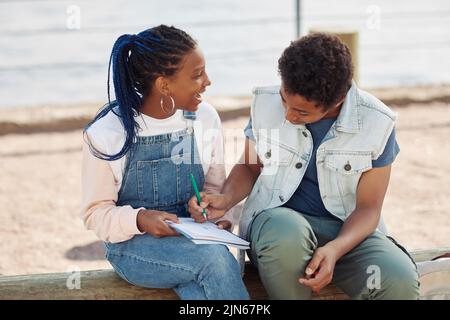 Portrait de deux adolescents noirs souriants qui apprécient les cours en extérieur et écrivent dans un carnet Banque D'Images
