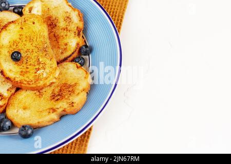 Toasts français au miel et aux myrtilles sur une assiette bleue sur fond blanc avec espace de copie. Pains grillés pour le petit déjeuner. Dessert sucré traditionnel Banque D'Images