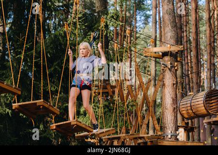 Une fille passe un obstacle dans une ville de corde. Une fille dans un parc de corde de forêt Banque D'Images