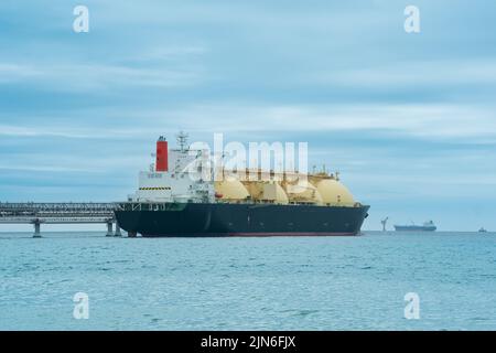 Camion-citerne de transport de gaz naturel liquéfié pendant le chargement à un terminal offshore de GNL, à la distance où le terminal d'exportation de pétrole est visible dans la mer Banque D'Images