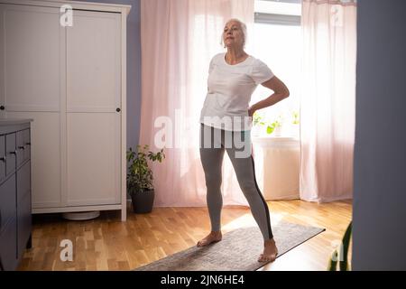 Femme senior faisant du yoga asana dans le salon. Banque D'Images