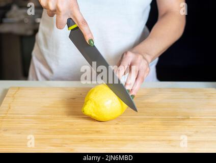 Gros plan de la jeune femme mains coupant citron sur bois coupant bo Banque D'Images