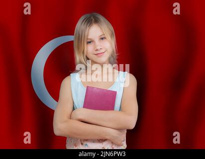 Jolie jeune fille tenant un livre sur fond de drapeau turc. Concept de l'école et de l'éducation en Turquie Banque D'Images