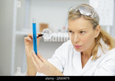 femme mature en blouse de laboratoire à l'aide d'une loupe Banque D'Images