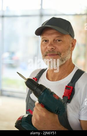 Portrait d'un constructeur barbu avec perceuse dans ses mains Banque D'Images